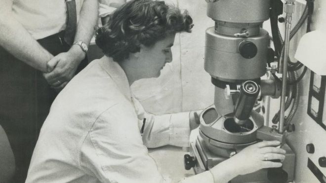 June Almeida mirando el microscopio